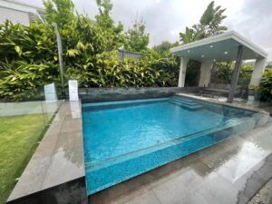 A modern pool with a glass wall, complemented by a gazebo, set in a peaceful outdoor environment lluide you through each stage, from design and approvals to construction and handover.